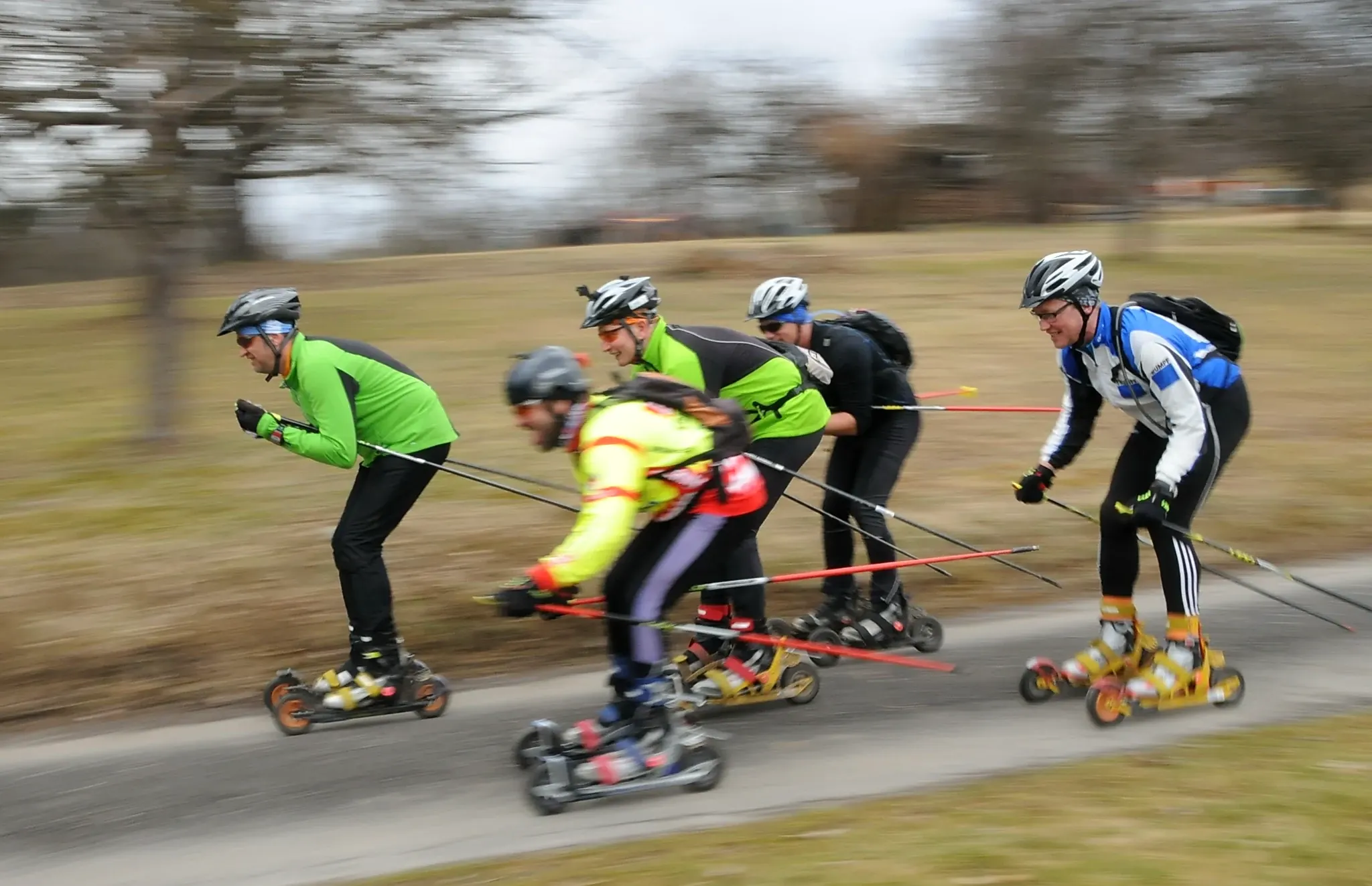 Gruppe auf Cross Skates mit Stöcken in voller Fahrt auf einem Feldweg